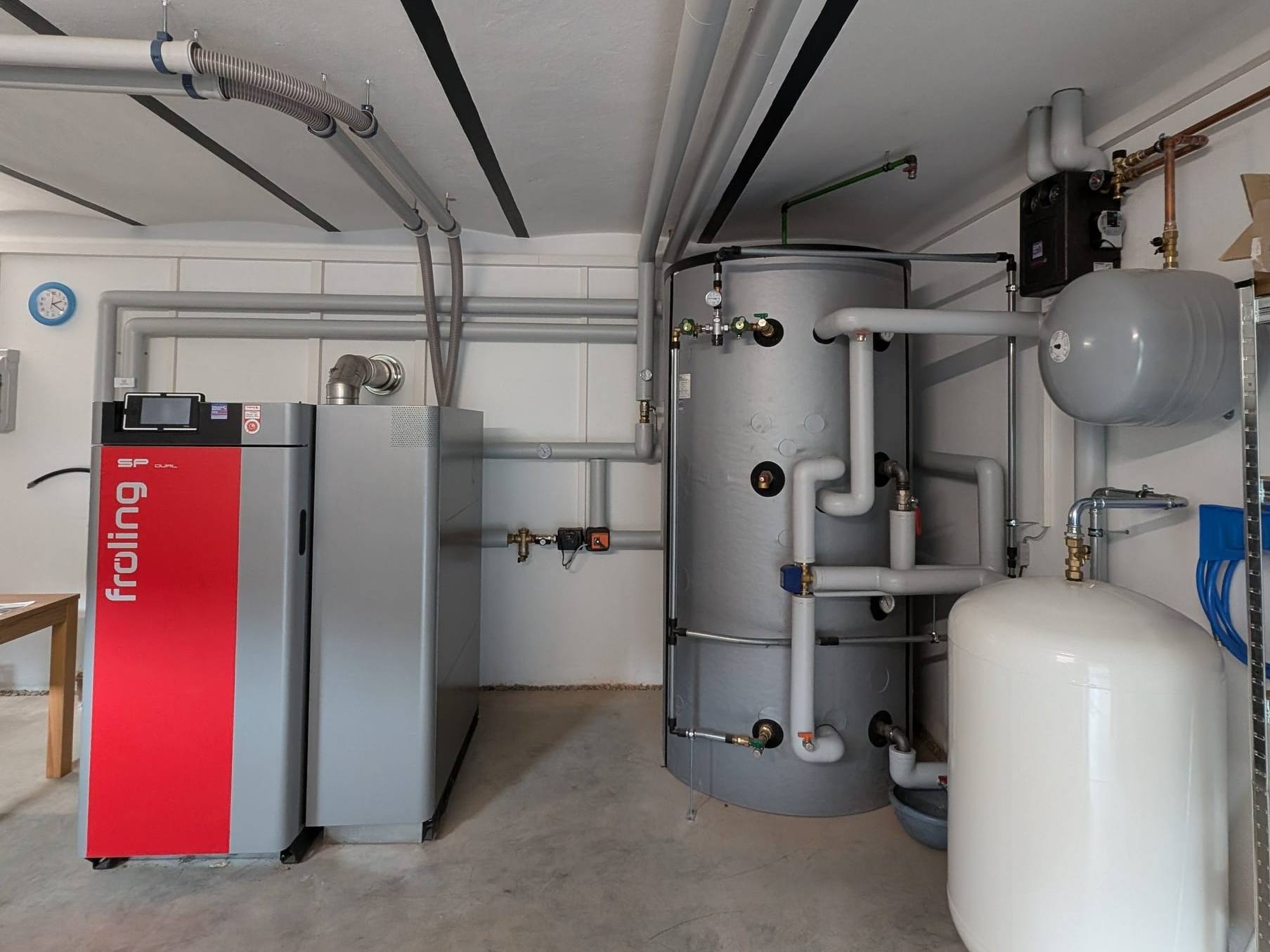 Heller Heizraum mit Fröling-SP-Dual-Kombikessel, grauem Pufferspeicher und Ausdehnungsgefäßen