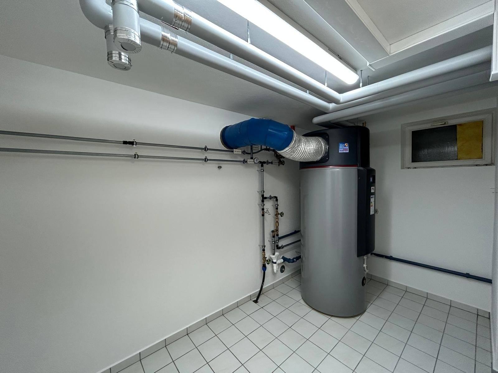 Aufgeräumter Technikraum mit Warmwasser-Wärmepumpe und blauem Luftkanal