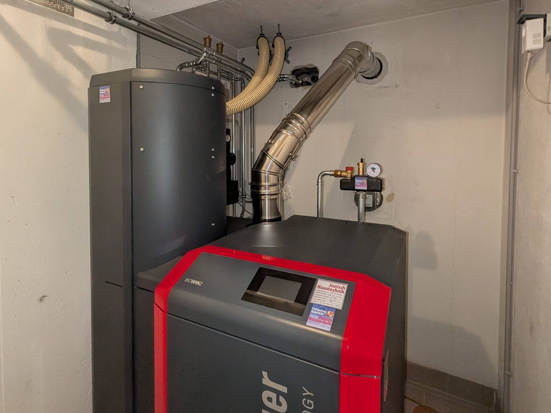 Windhager-Pelletskessel BioWIN2 mit Saugschläuchen und Edelstahl-Abgasrohr im Heizraum