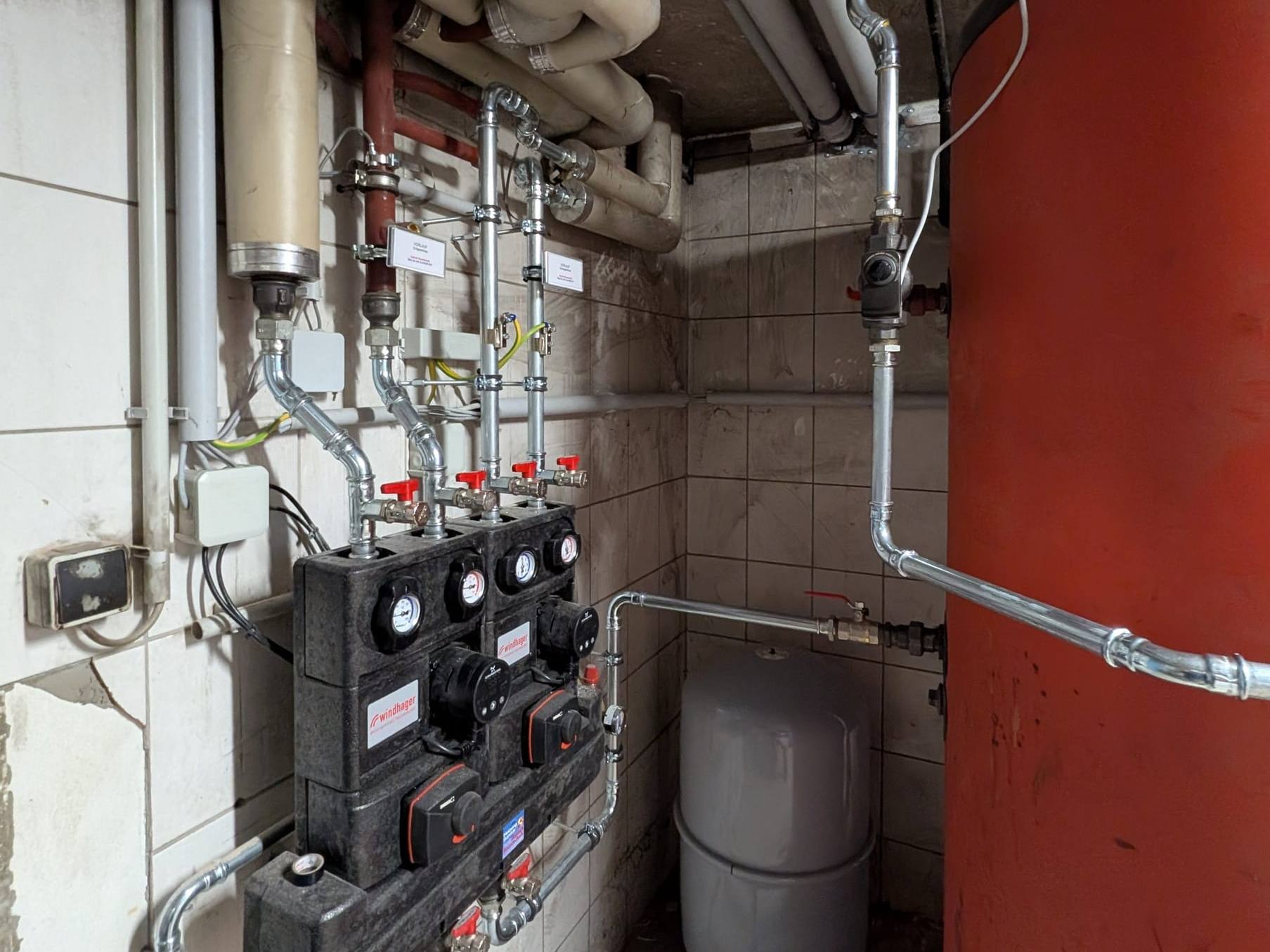 Neue Heizkreis-Pumpengruppen mit Mischern neben rotem Pufferspeicher im Heizraum