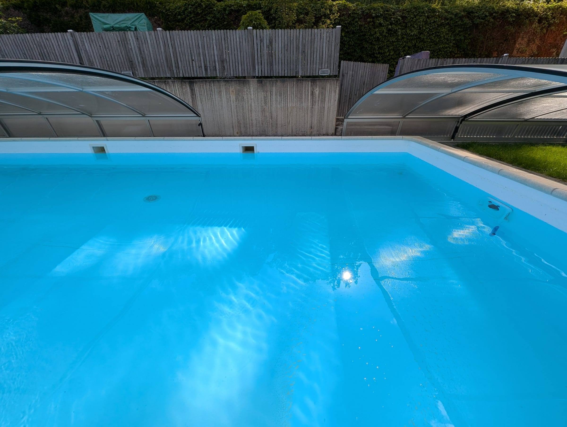 Klares, hellblaues Poolbecken mit zurückgeschobener Überdachung und Holzzaun