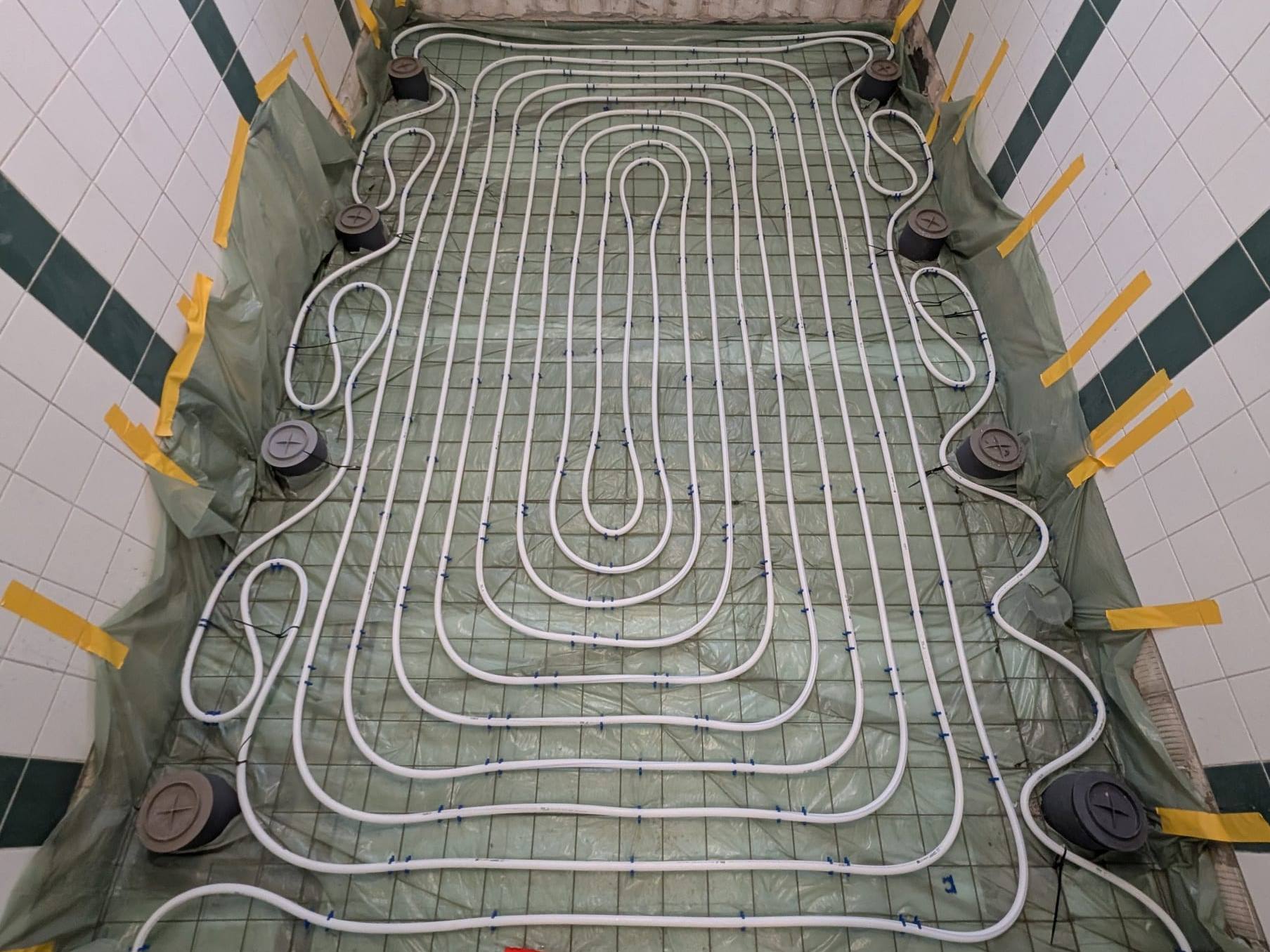 Fußbodenheizungsrohre in Schleifen auf Baustahlmatte in einer gefliesten Gemeinschaftsdusche mit Bodenabläufen