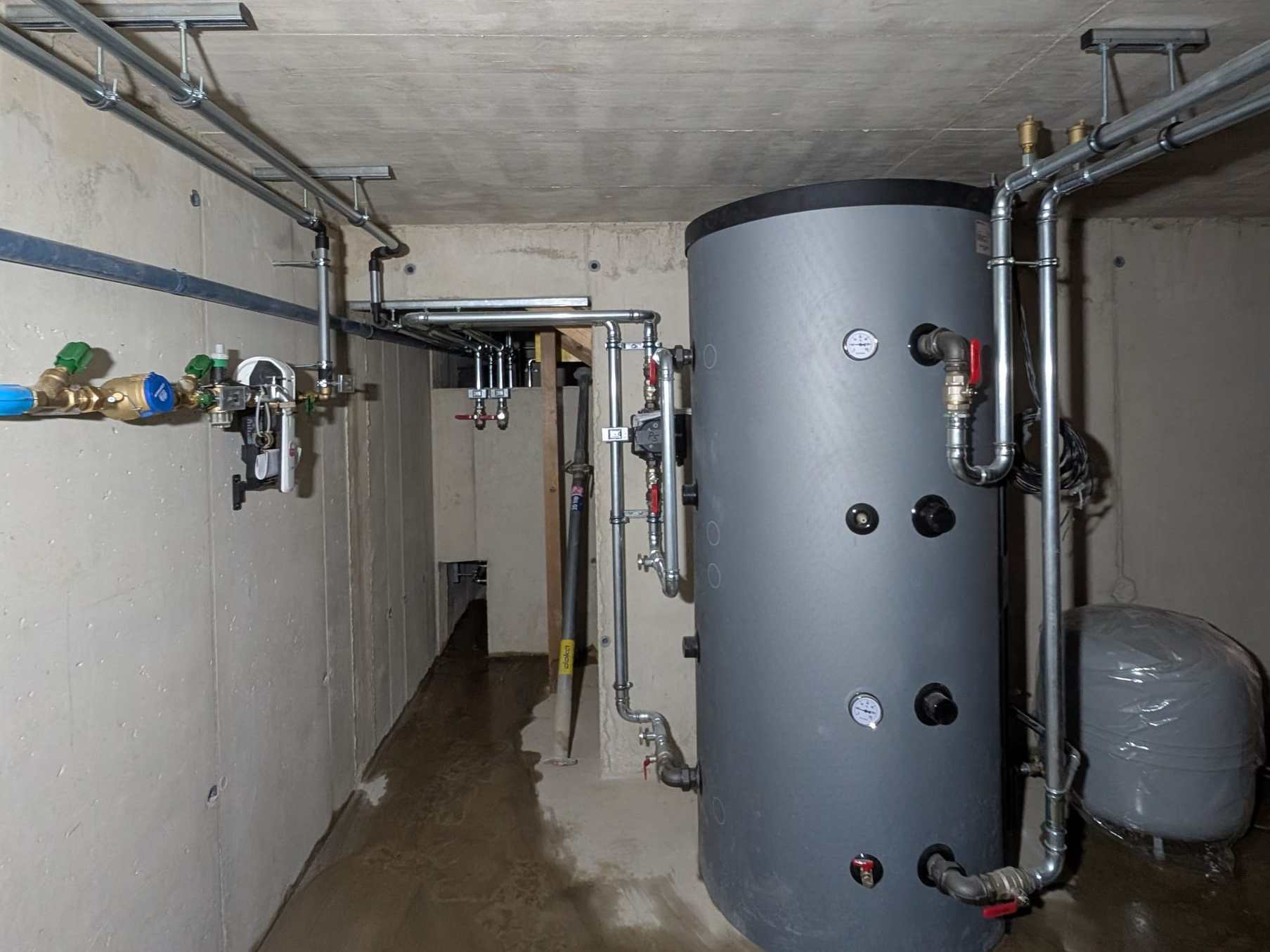 Grau gedämmter Pufferspeicher mit verzinkten Leitungen in einem neuen Betonkeller