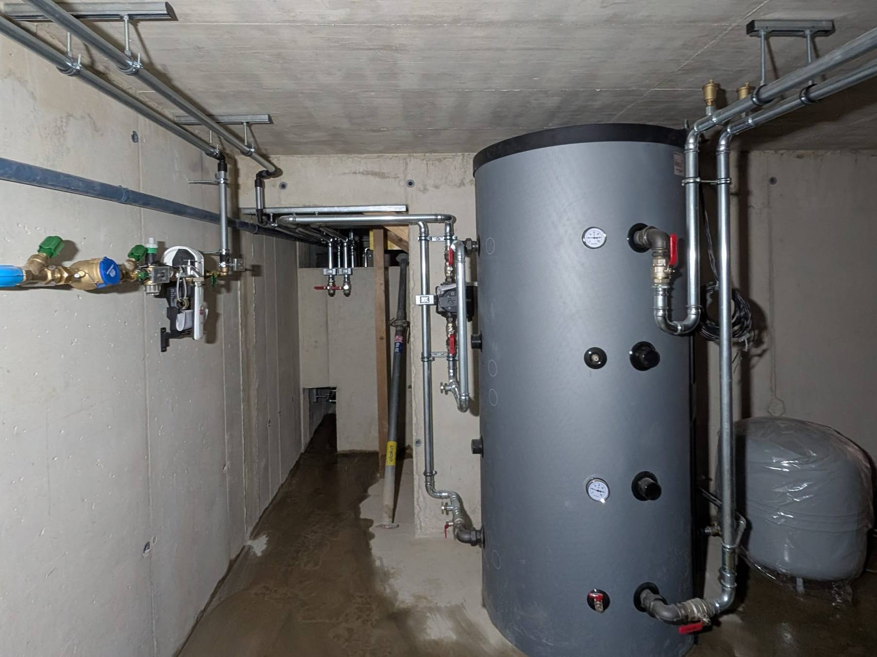Grau gedämmter Pufferspeicher mit verzinkten Leitungen in einem neuen Betonkeller