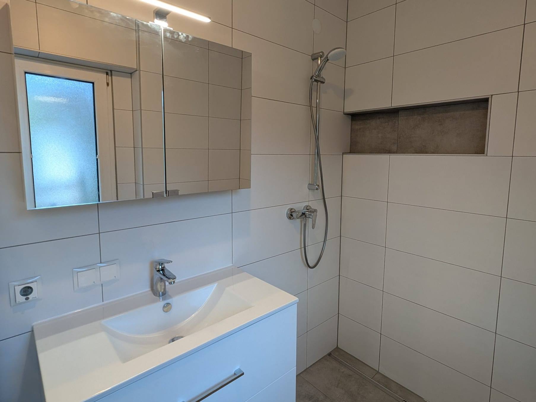 Bad mit bodengleicher Dusche, Duschrinne, Wandnische und weißem Waschtisch mit Spiegelschrank