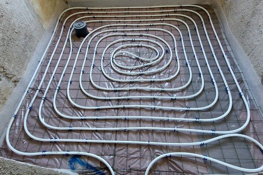 Schneckenförmig verlegte Fußbodenheizung mit Bodenablauf in einem Raum im Rohbau