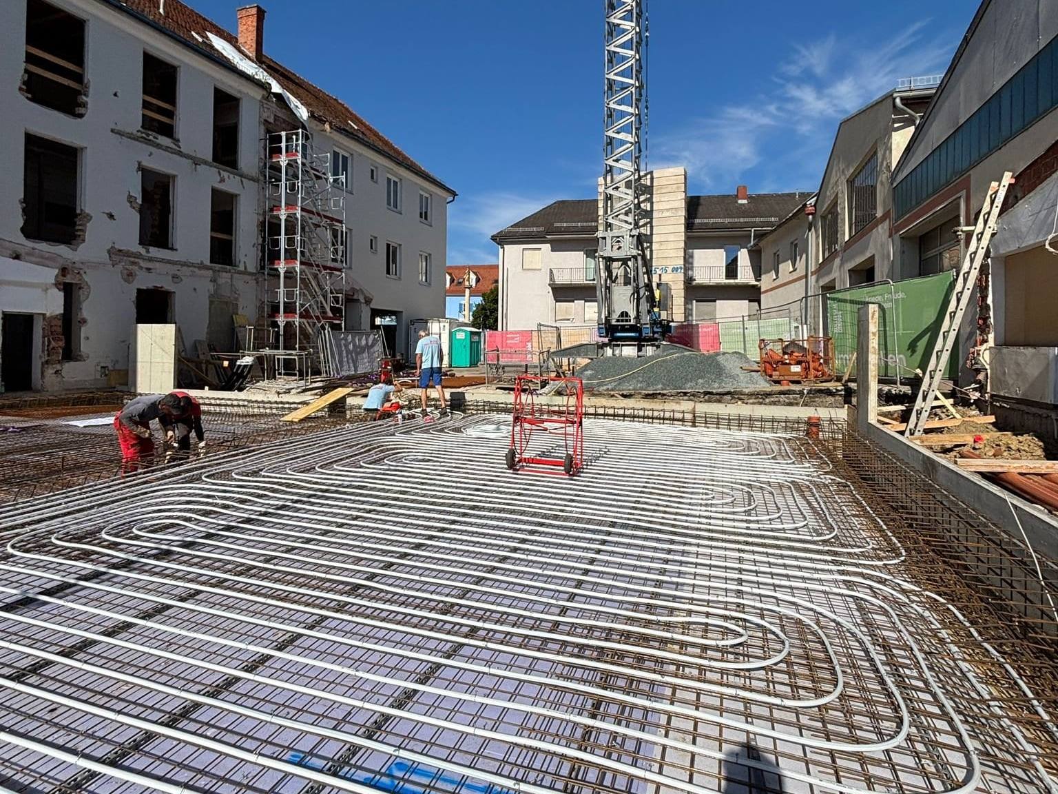 Großflächig verlegte Rohre der Betonkernaktivierung auf der Bewehrung der Bodenplatte, dahinter ein Baukran