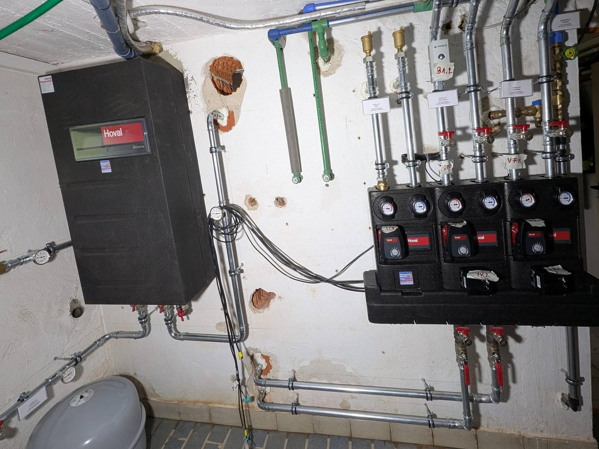 Heizraum mit Hoval-Belaria-Inneneinheit und drei Heizkreis-Pumpengruppen an verrohrtem Verteiler