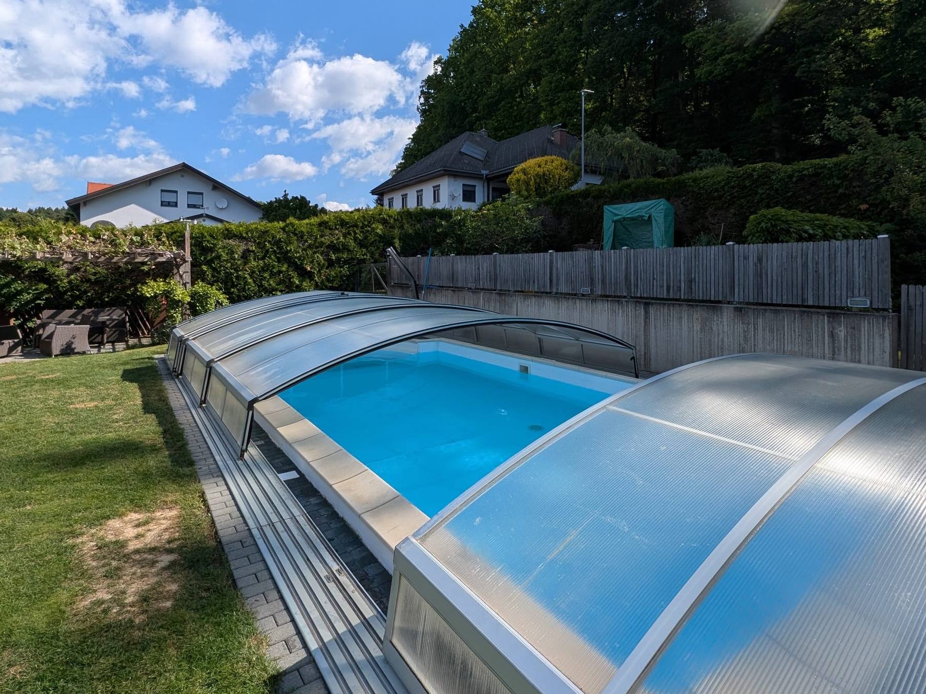 Gartenpool mit transparenter Teleskop-Überdachung, Rasen und Holzzaun an einem Sommertag