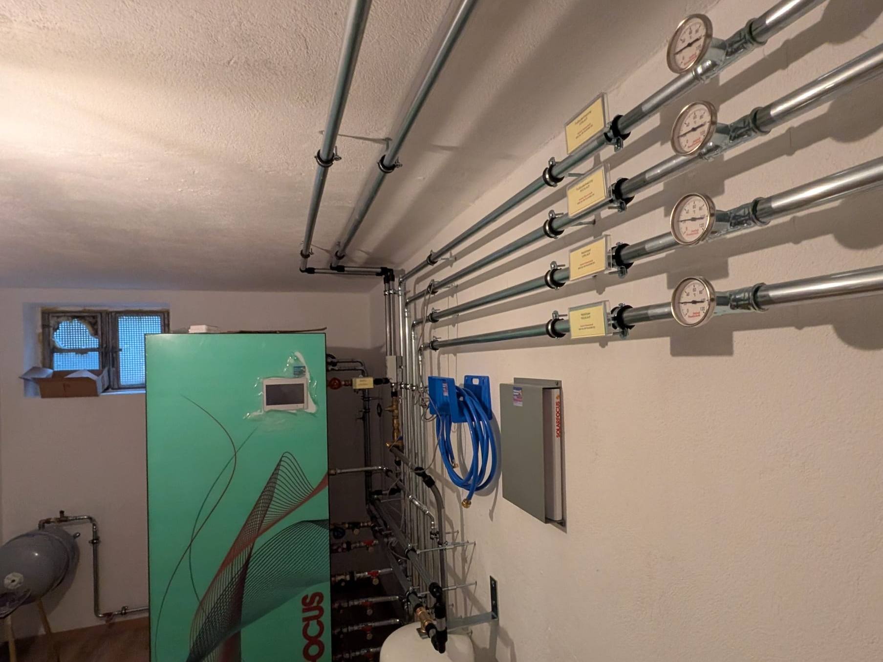 Verzinkte Heizkreisleitungen mit Thermometern und Beschriftung neben einem grünen Solarfocus-Gerät