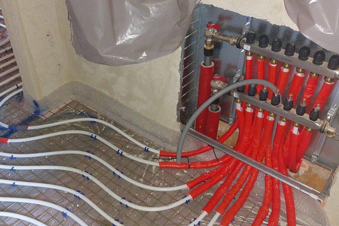 Heizkreisverteiler mit rot isolierten Anschlüssen und verlegter Fußbodenheizung