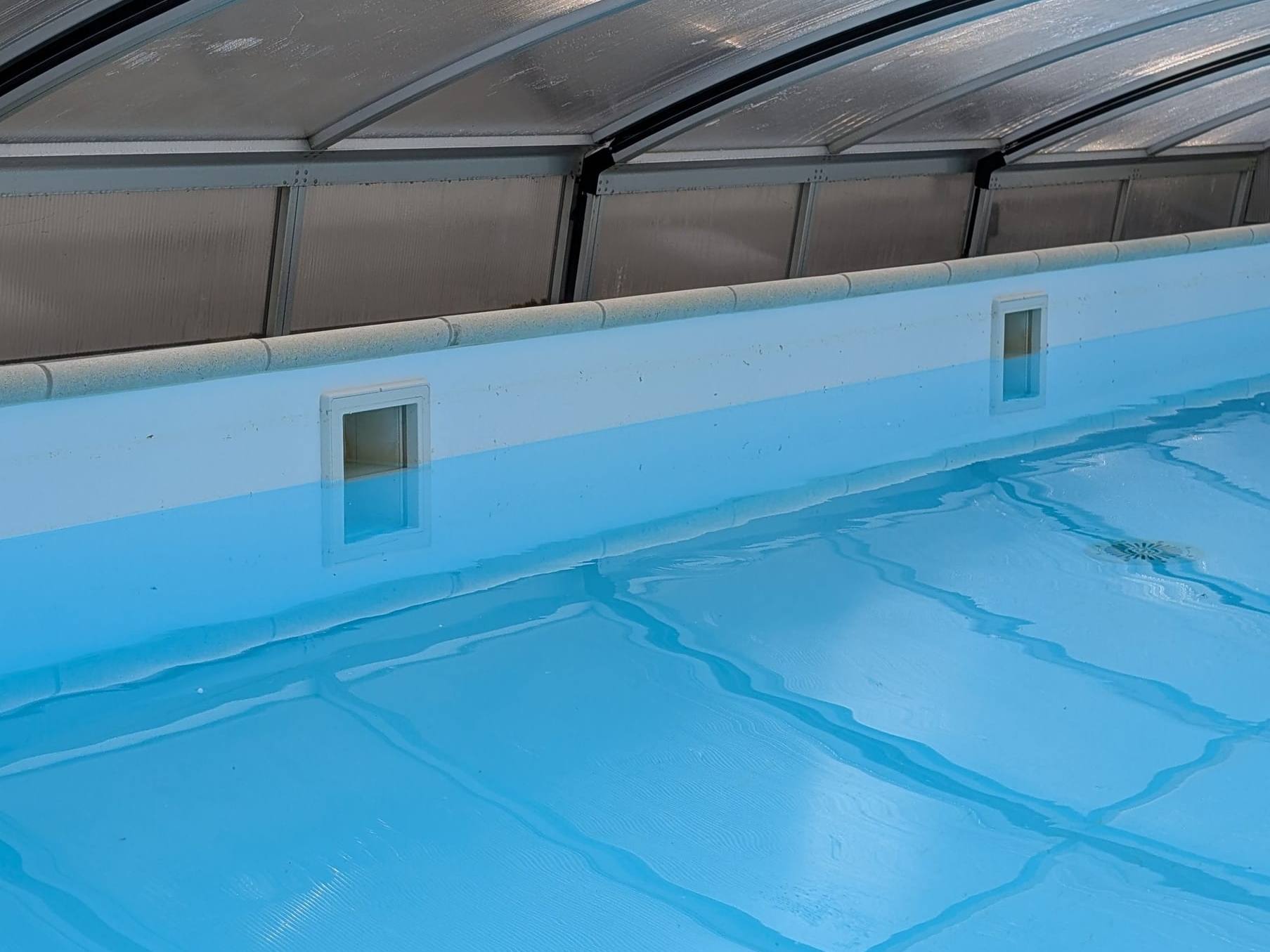 Hellblaues Poolwasser unter einer gewölbten, transparenten Überdachung