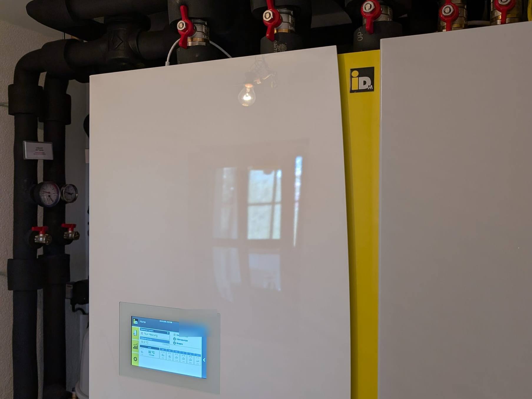 Touch-Display an der weißen Front einer Wärmepumpe, darüber gedämmte Leitungen mit roten Kugelhähnen