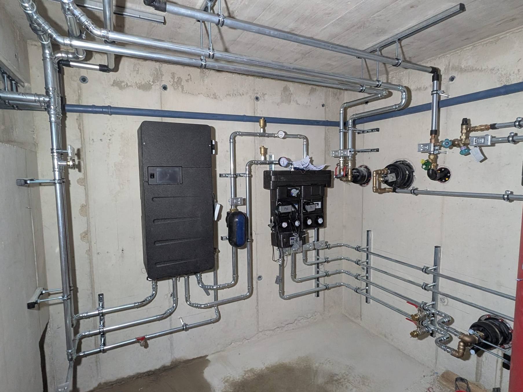 Schwarz gedämmtes Wandmodul und Pumpengruppen mit verzinkter Verrohrung an einer Betonwand