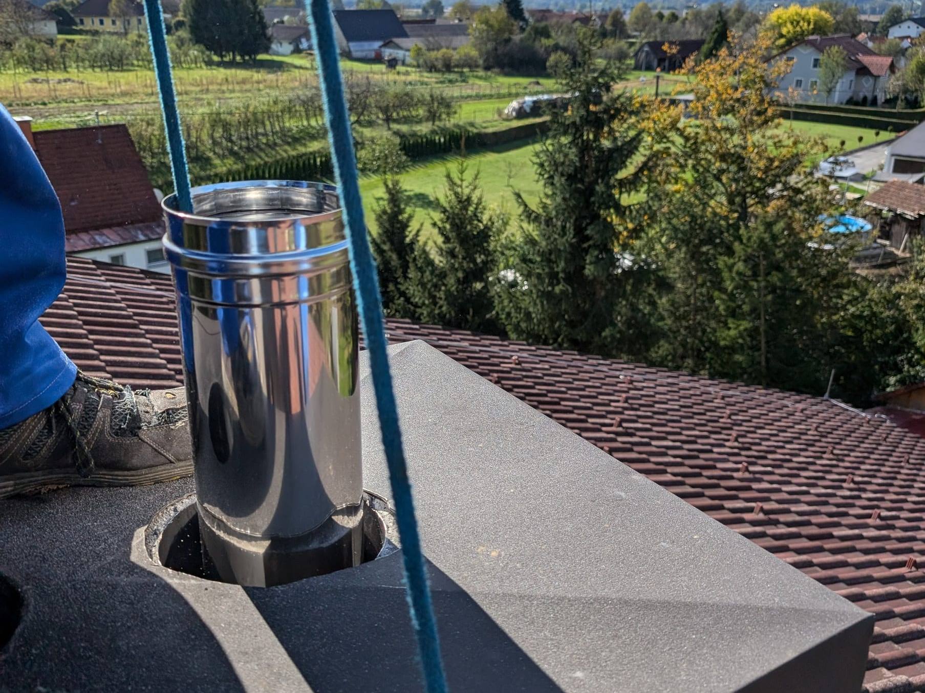 Edelstahl-Abgasrohr in der Kaminabdeckung auf einem Ziegeldach, dahinter eine herbstliche Hügellandschaft