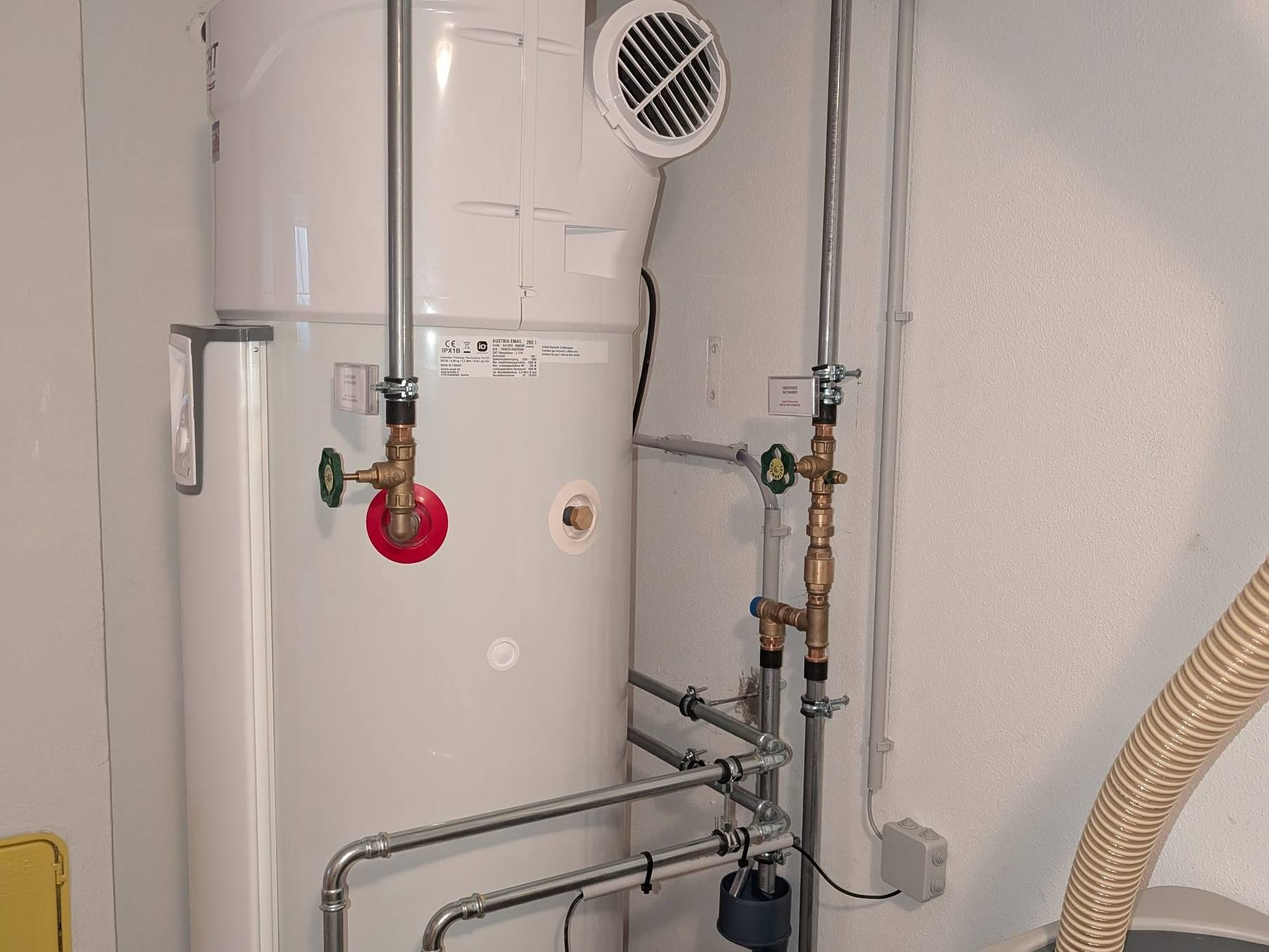 Warmwasser-Wärmepumpe mit Luftgitter und verpressten Rohrleitungen im Heizraum