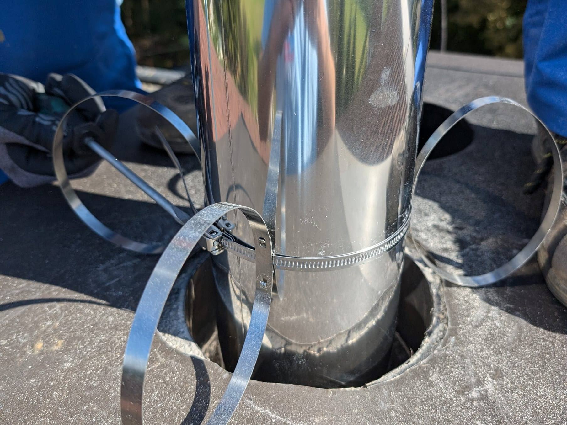 Edelstahl-Abgasrohr mit Spannbändern in der Kaminöffnung, daneben Monteure in blauer Arbeitskleidung