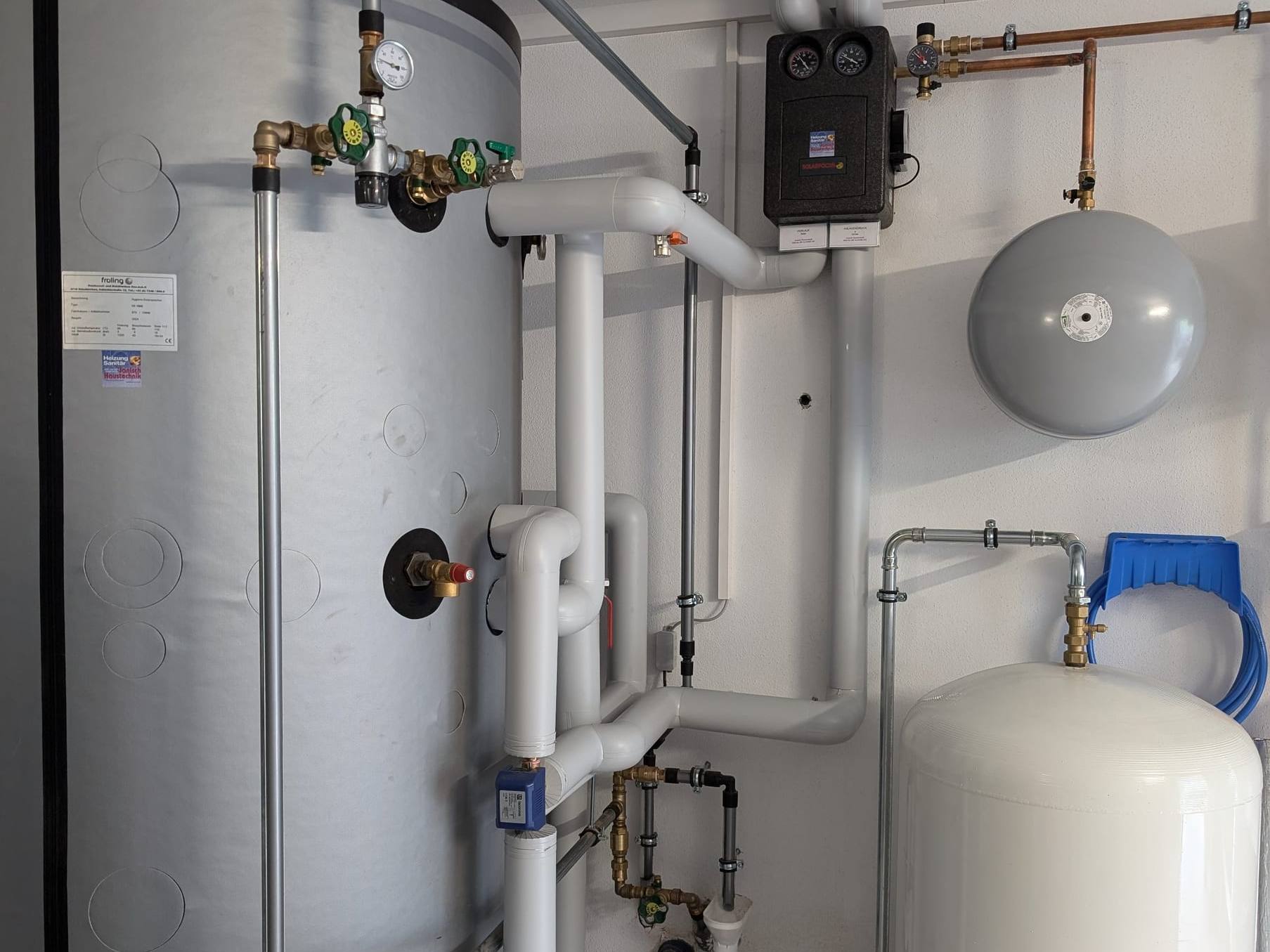 Grauer Speicher mit gedämmten Anschlussleitungen, Pumpenstation und Ausdehnungsgefäßen im Heizraum
