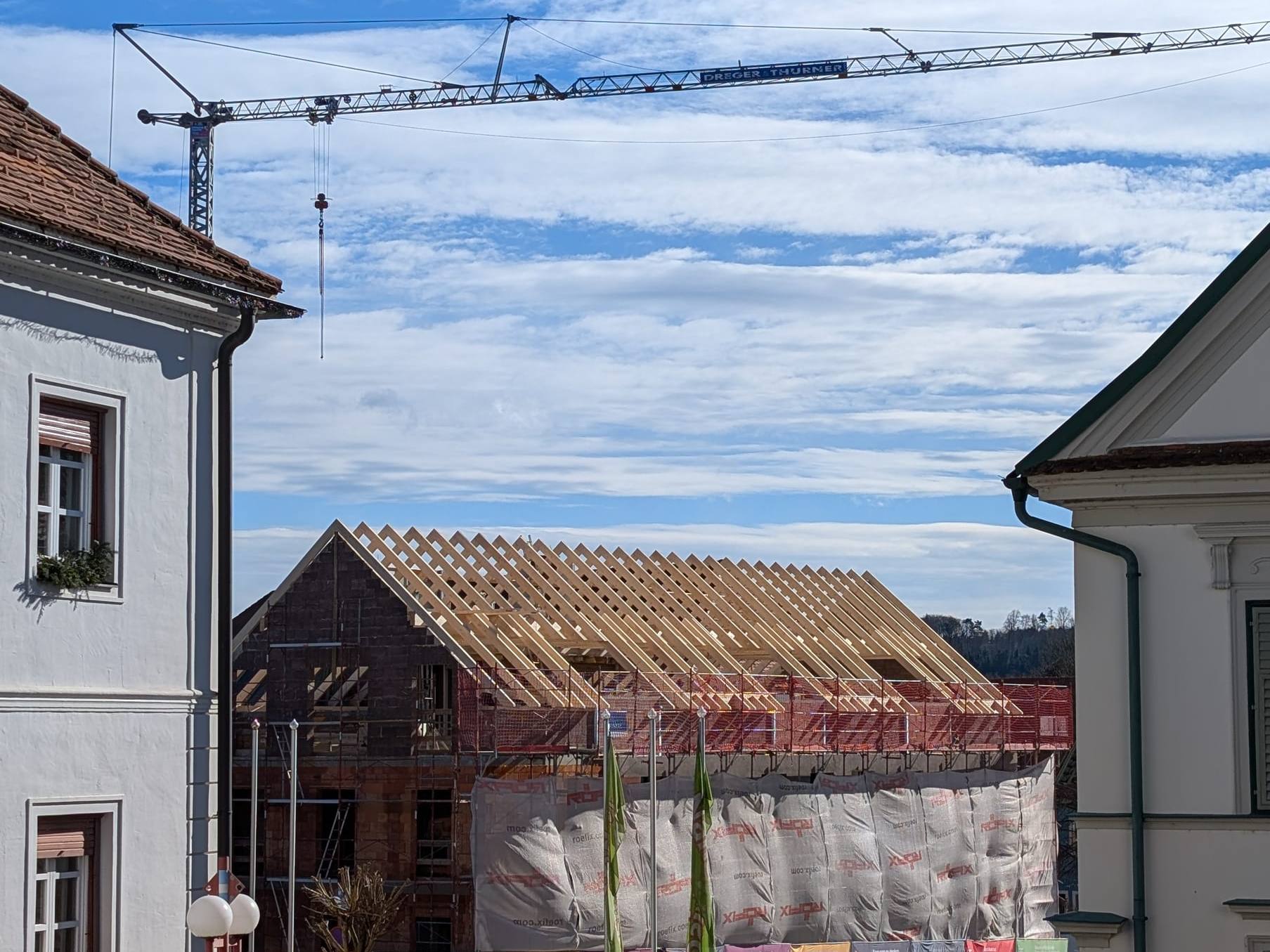Neuer Dachstuhl aus Holz zwischen den Altbauten, dahinter ein Baukran