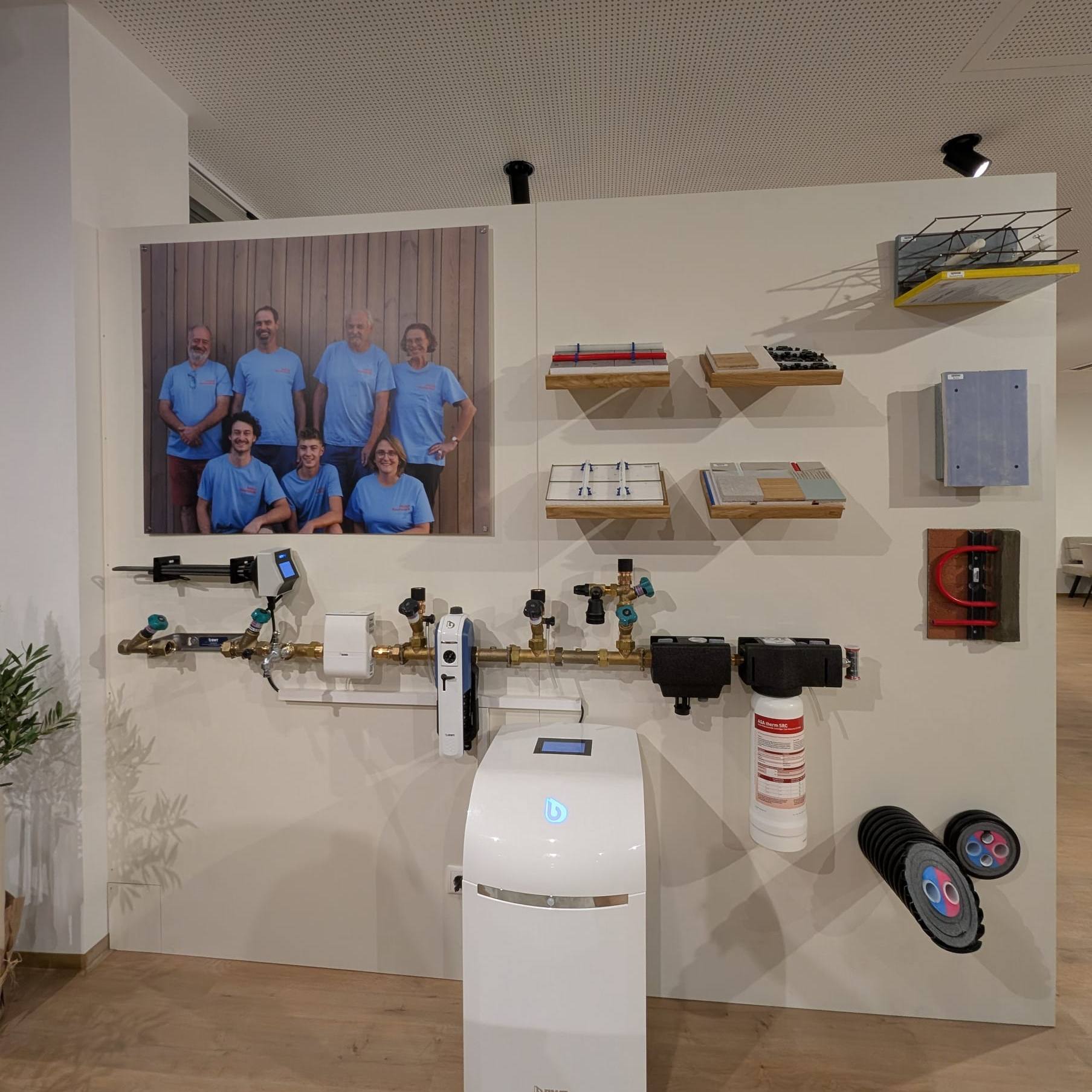 BWT-Trinkwasserlinie mit Filter und weißer Enthärtungsanlage an der Wand unseres Schauraums, darüber ein Teamfoto