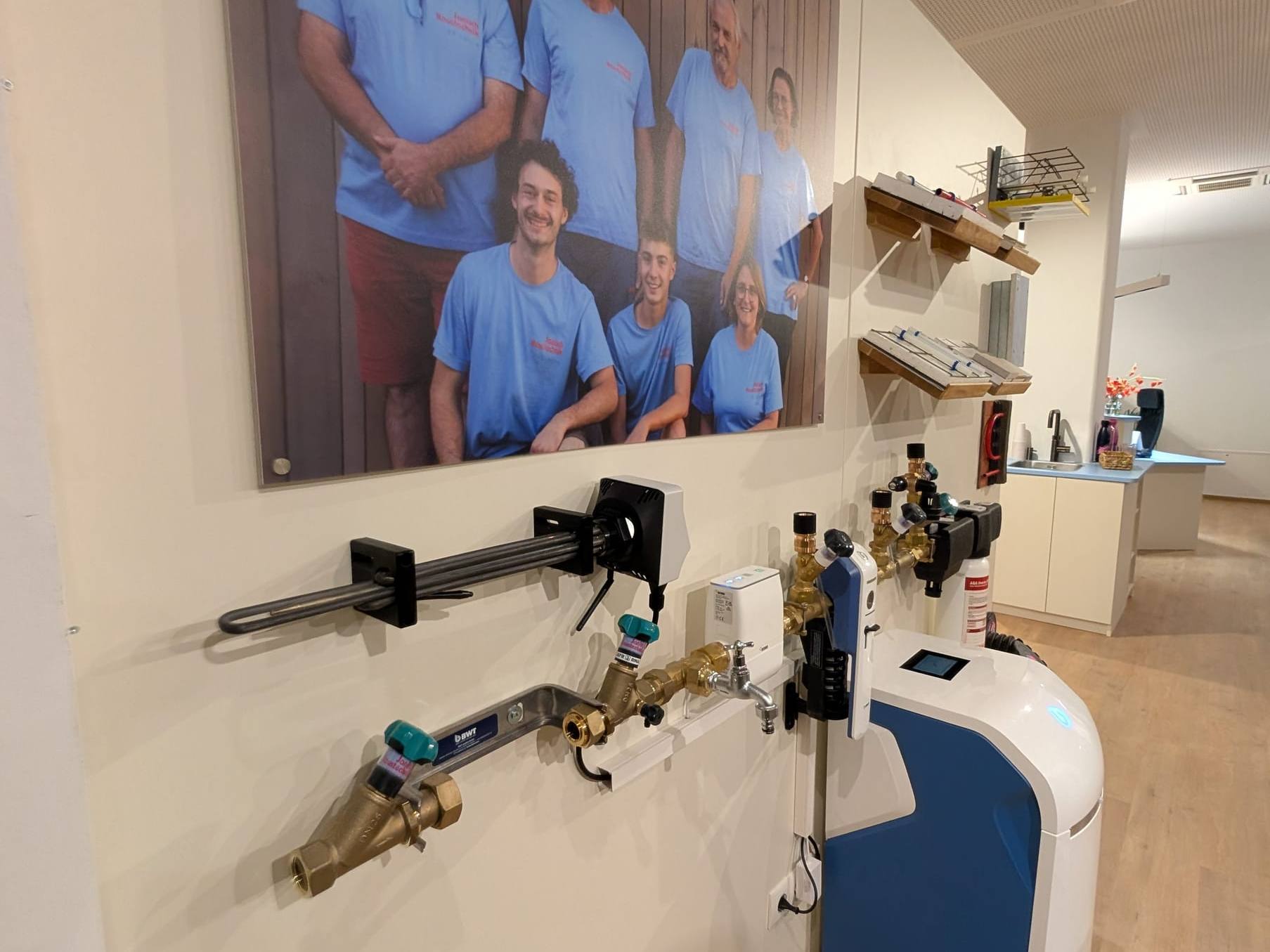 Armaturen und Fittings an der Wand vor einem großen Teamfoto in blauen T-Shirts