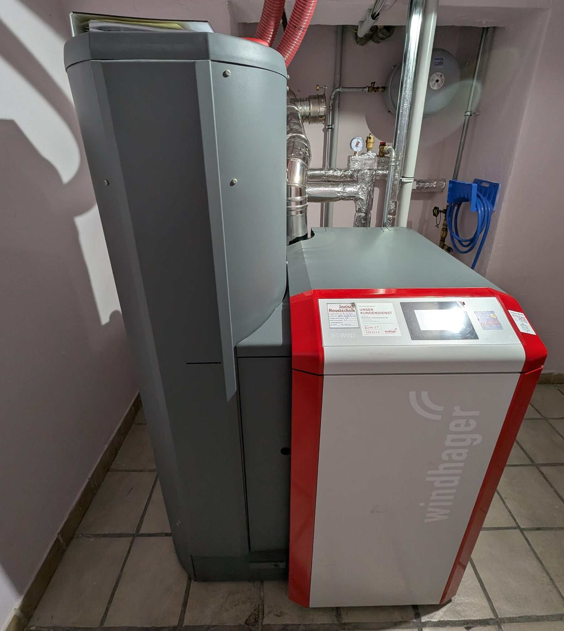Pelletskessel BioWIN2 von Windhager mit Vorratsbehälter und Saugschläuchen in einem gefliesten Heizraum