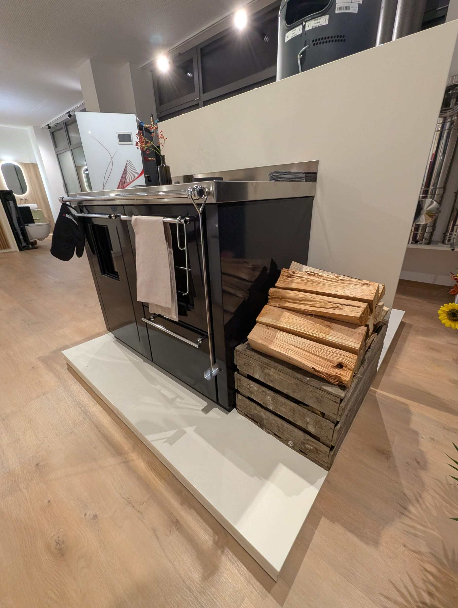 Holzküchenherd mit Edelstahlplatte und einer Kiste Brennholz in unserem Schauraum in Ilz