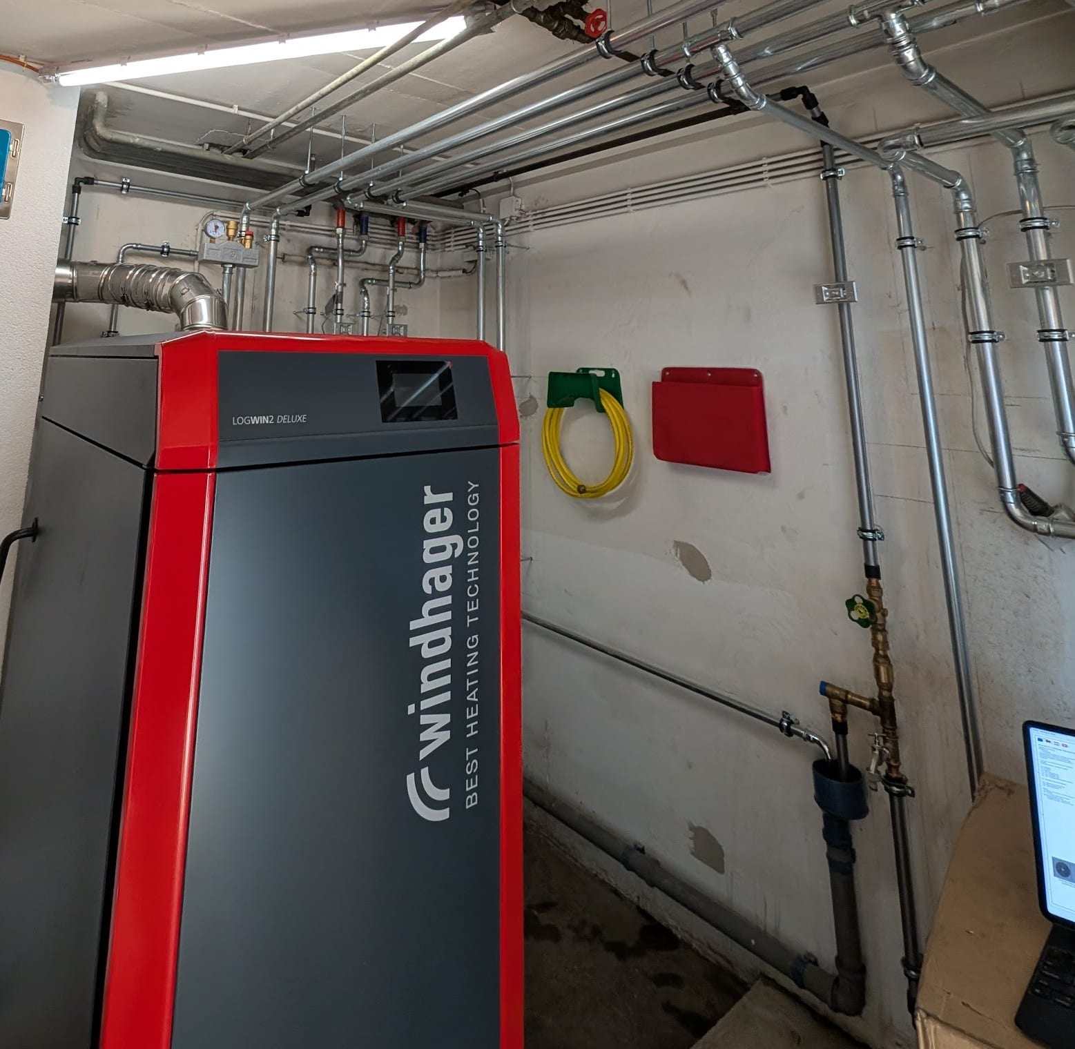 Stückholzkessel Windhager LogWIN2 DELUXE in einem hellen Heizraum mit sauber verlegten Rohrleitungen