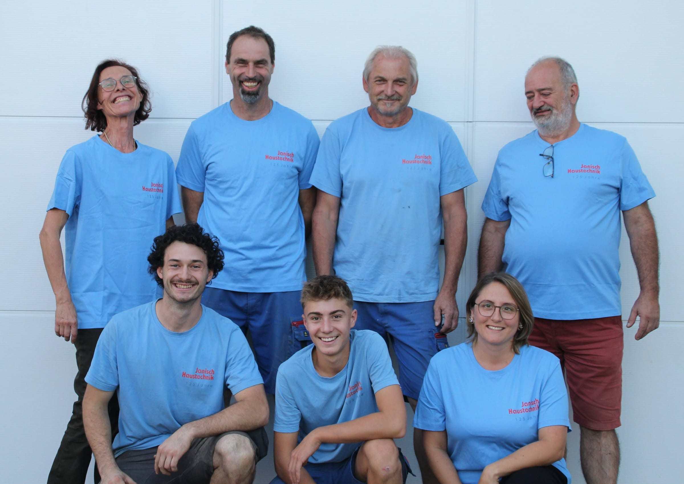 Das Team von Janisch Haustechnik in hellblauen T-Shirts vor einem weißen Garagentor, vorne drei kniend