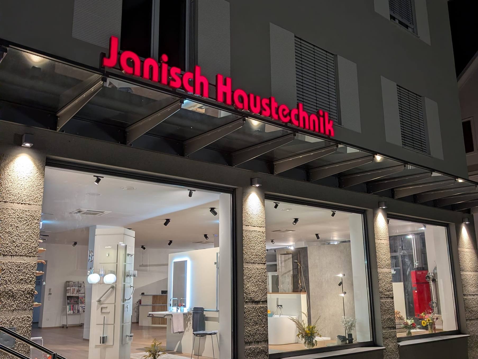 Der neue Schauraum von Janisch Haustechnik am Abend, mit rotem Schriftzug über den beleuchteten Schaufenstern