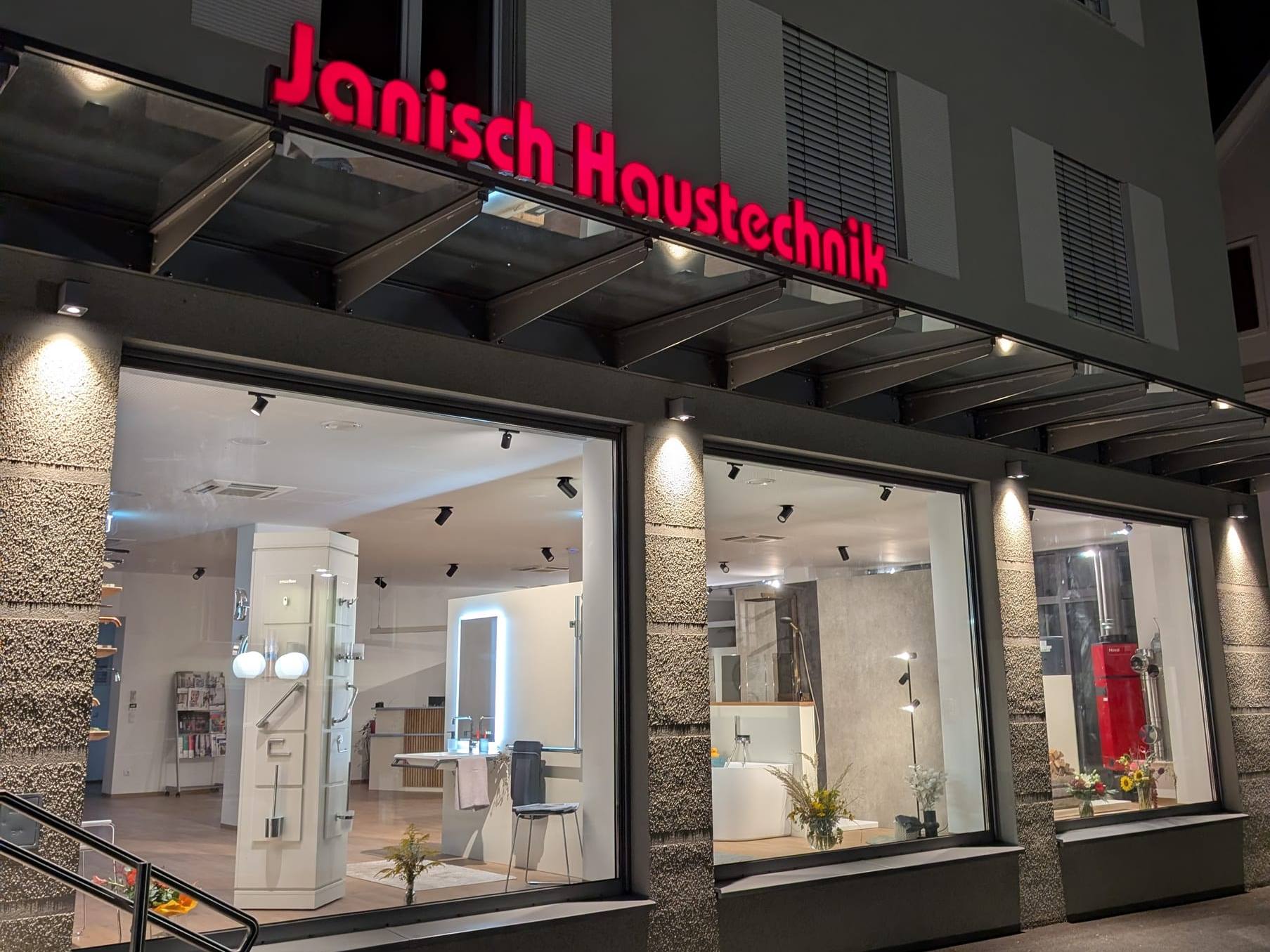 Der neue Schauraum von Janisch Haustechnik in Ilz 150 am Abend, mit rotem Schriftzug und beleuchteten Schaufenstern