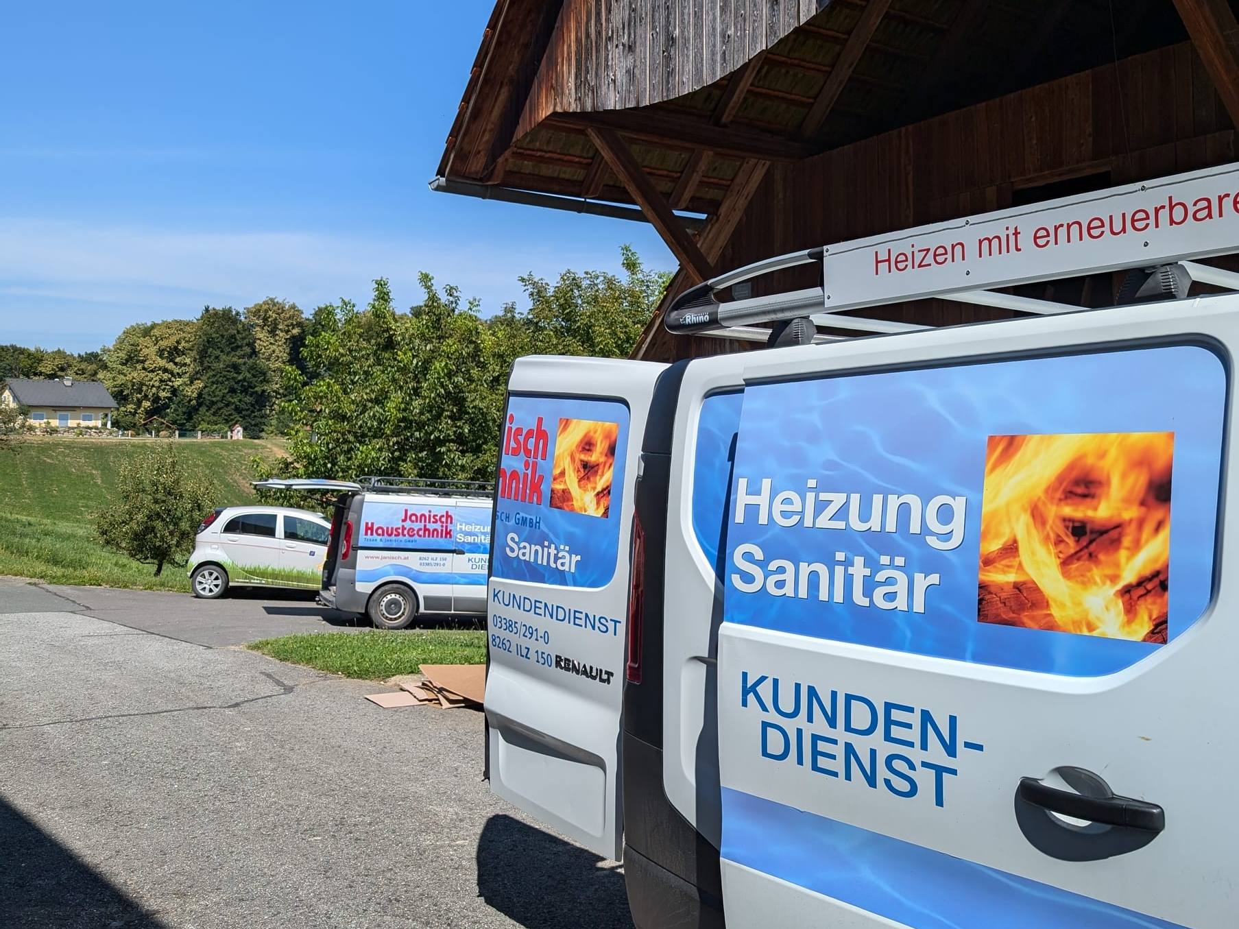 Weißer Kundendienst-Bus von Janisch Haustechnik mit der Aufschrift Heizung Sanitär Kundendienst vor einem Holzstadel