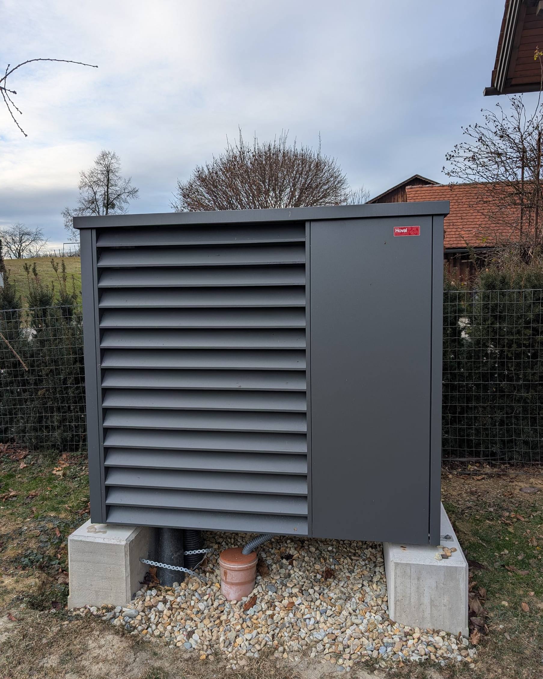 Luftwärmepumpe auf zwei Betonblöcken über einem Kiesbett im Garten