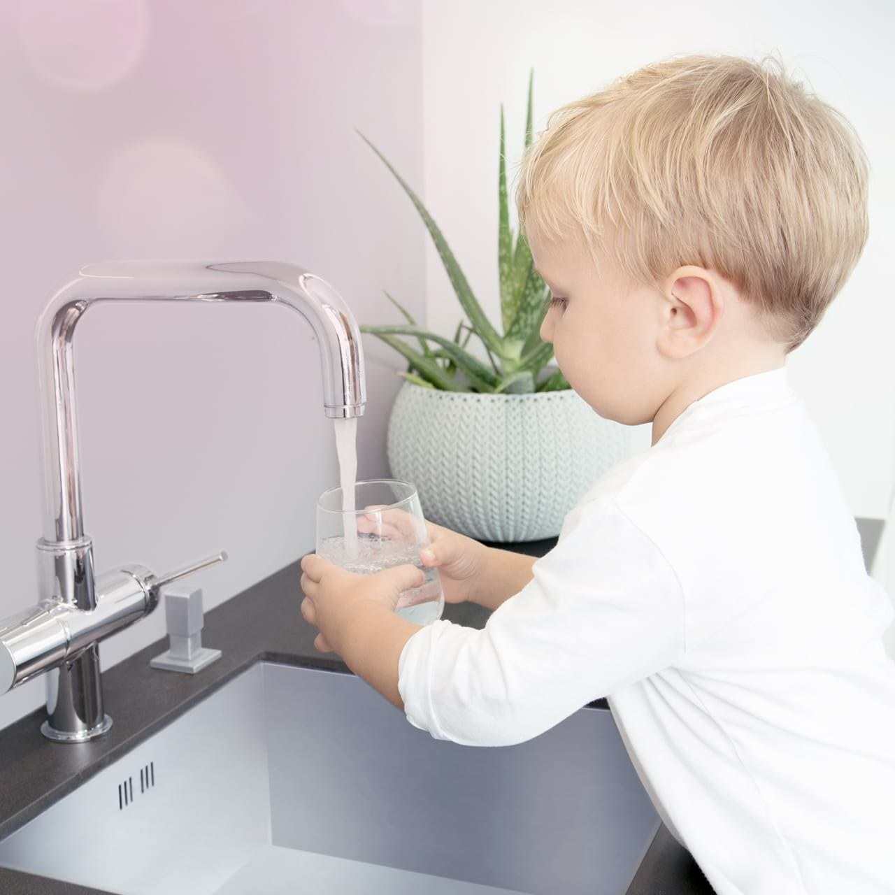 Ein Kind füllt an einer Küchenarmatur ein Glas mit klarem Leitungswasser, Herstellerbild von BWT